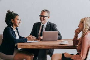 Two business professionals seated at a desk, discussing documents and working on a laptop during a meeting.