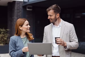 Two professionals reviewing a laptop while walking outdoors with coffee