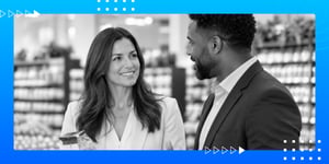 Black-and-white photo of a woman and man in business attire talking and smiling in a store aisle, with a blue decorative border