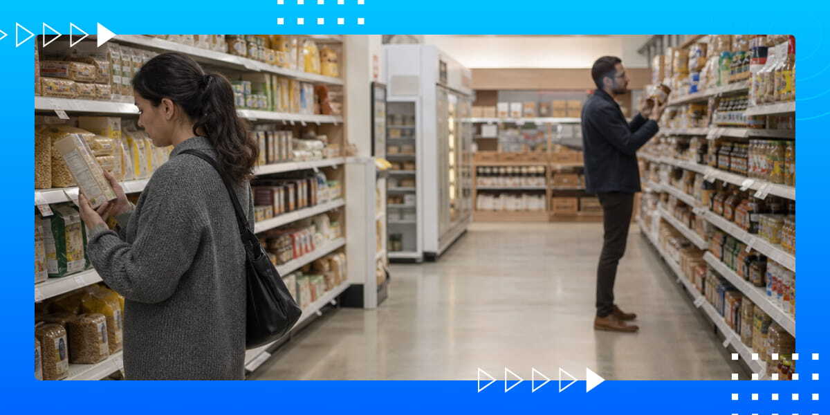Shoppers compare packaged food products in a grocery store aisle lined with shelves and refrigerated cases.