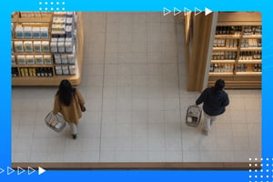 Overhead view of two shoppers carrying baskets while walking through a well-stocked grocery store aisle.