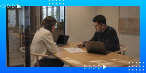 Two colleagues reviewing a document with laptops at a meeting table in a modern office.